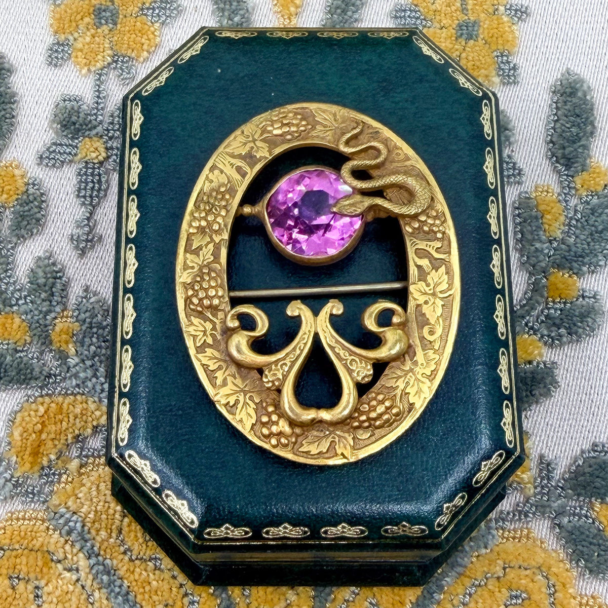 An gold-tone antique brooch with a snake and large pink stone