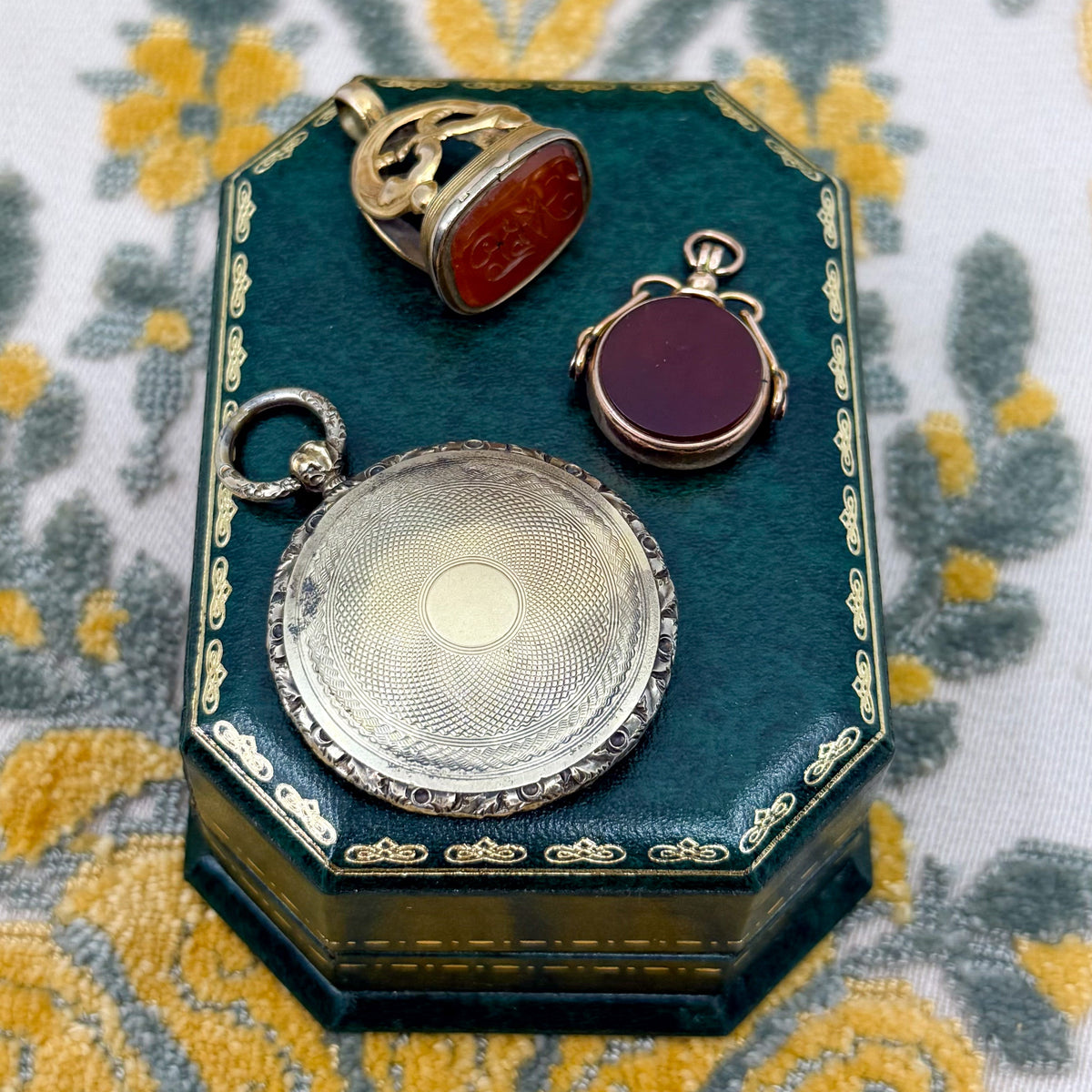 A collection of antique charms, lockets, and fobs on a green jewelry box