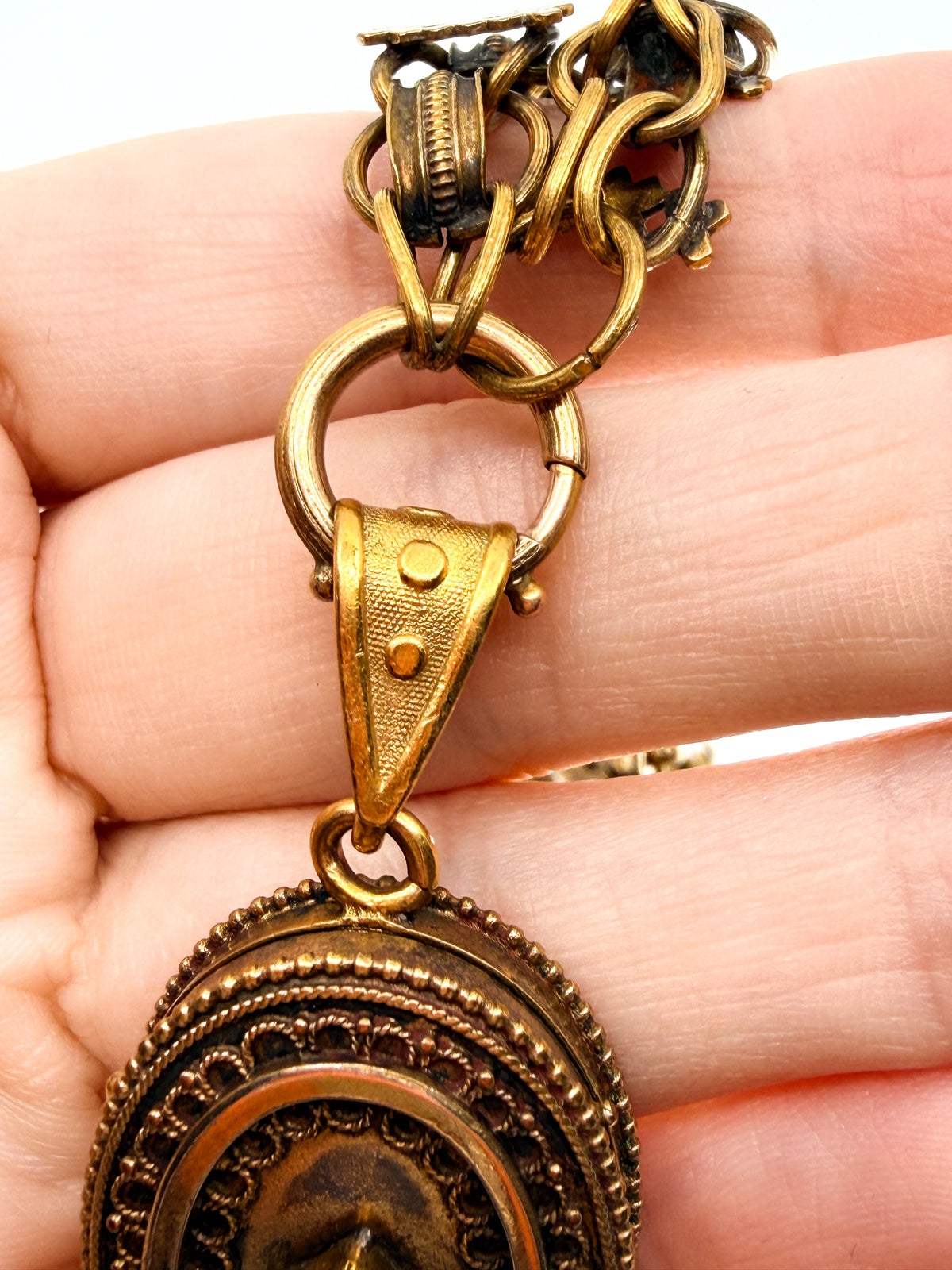 A close up of the spring ring closure on a Victorian book chain necklace with a locket hanging from it. 
